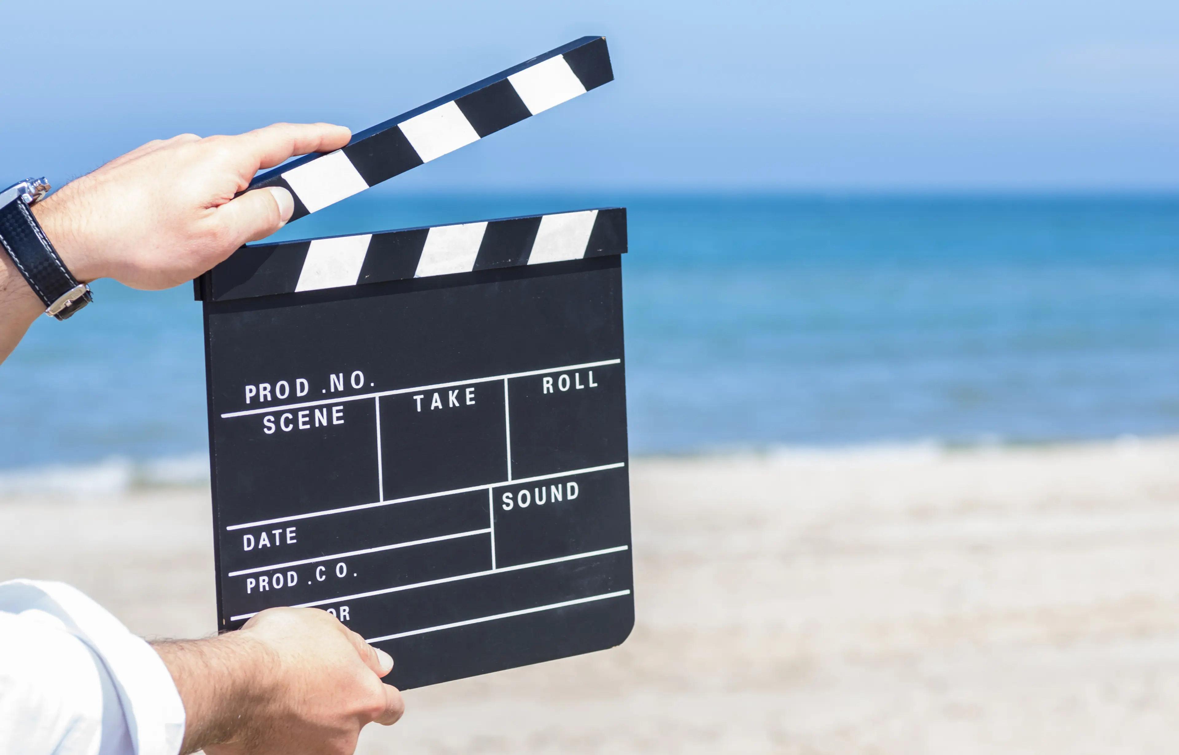 A pair of hands holding a clapboard with a beach faintly visible in the background