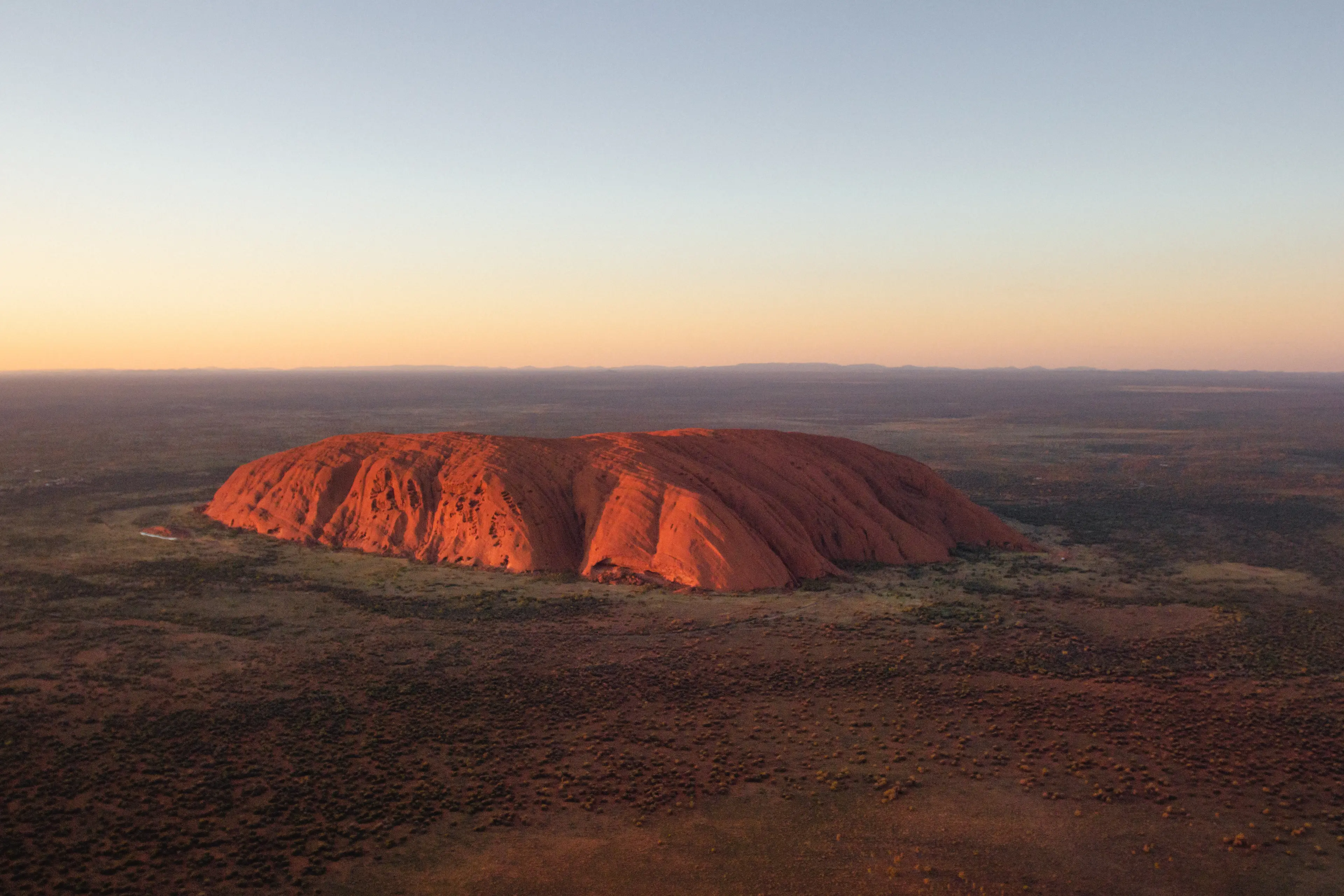 Panoramic view of the red colored Ayers Rock (Uluru) in the middle of the flat desert landscape of Uluru-Kata Tjuta National Park
