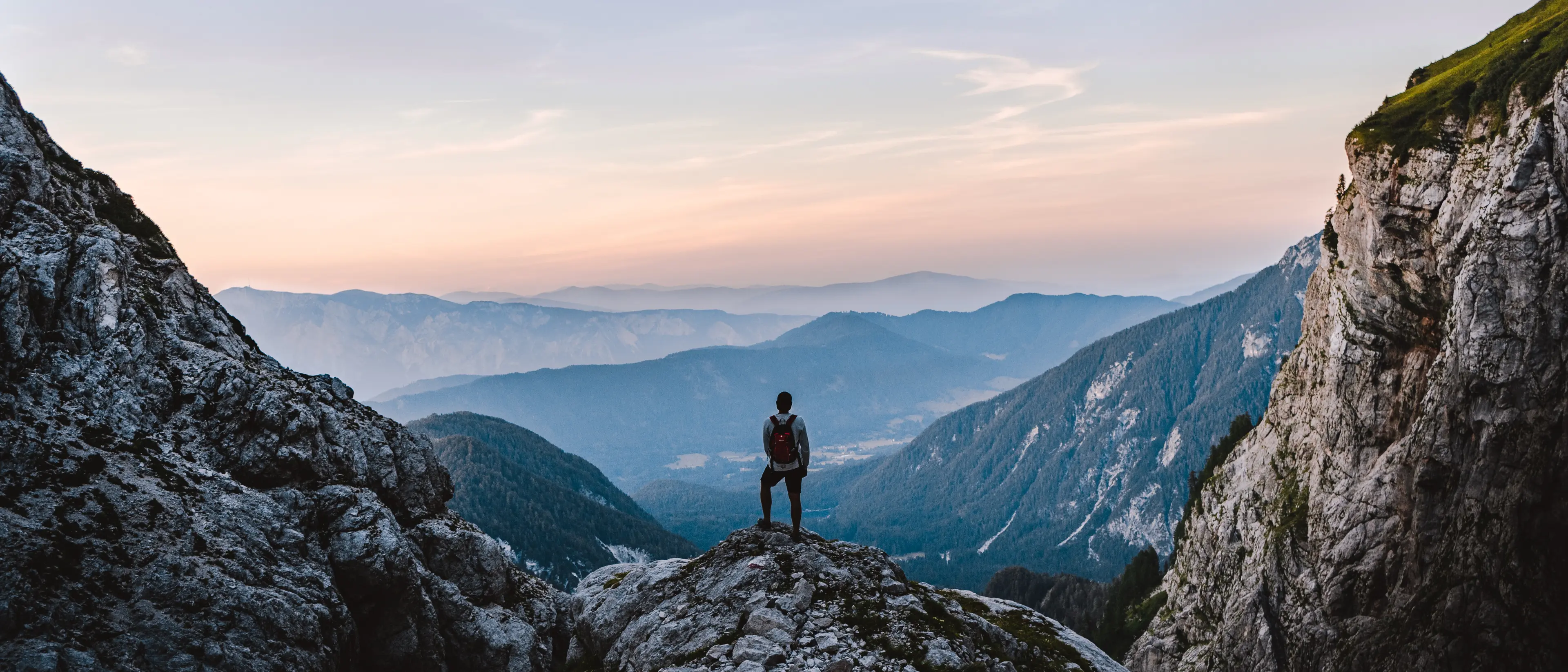 A hiker overlooking a majestic mountainous landscape from up high.