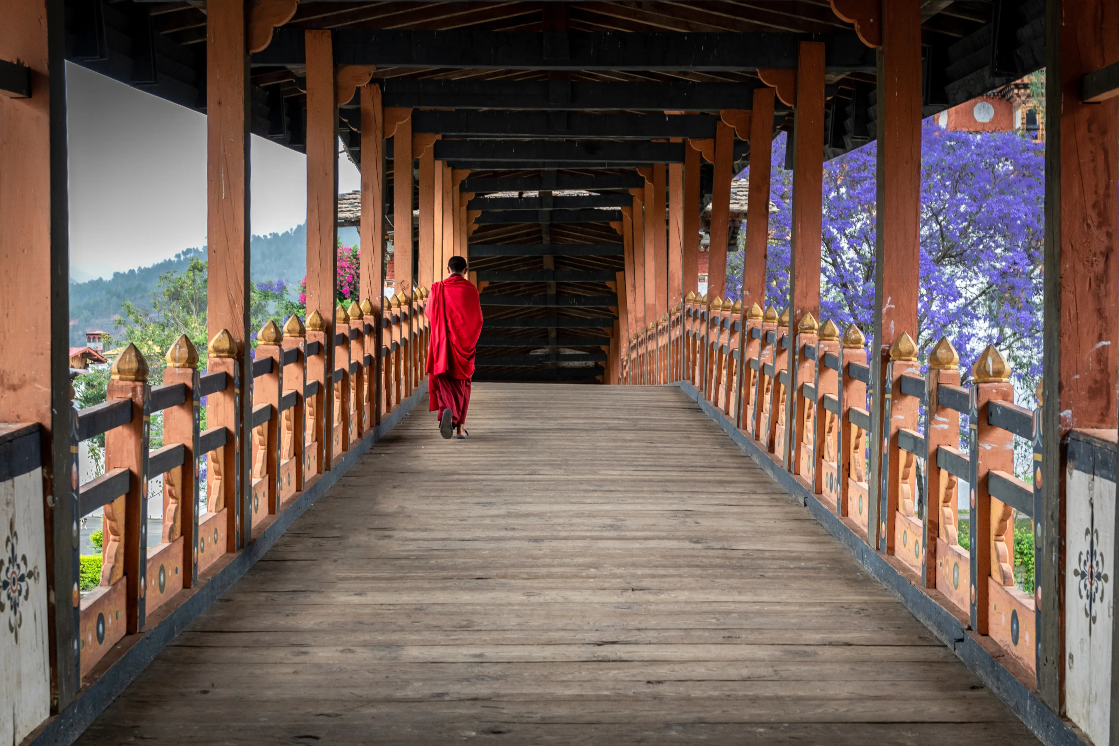 A monk dressed in a red robe walking around Punakha Dzong