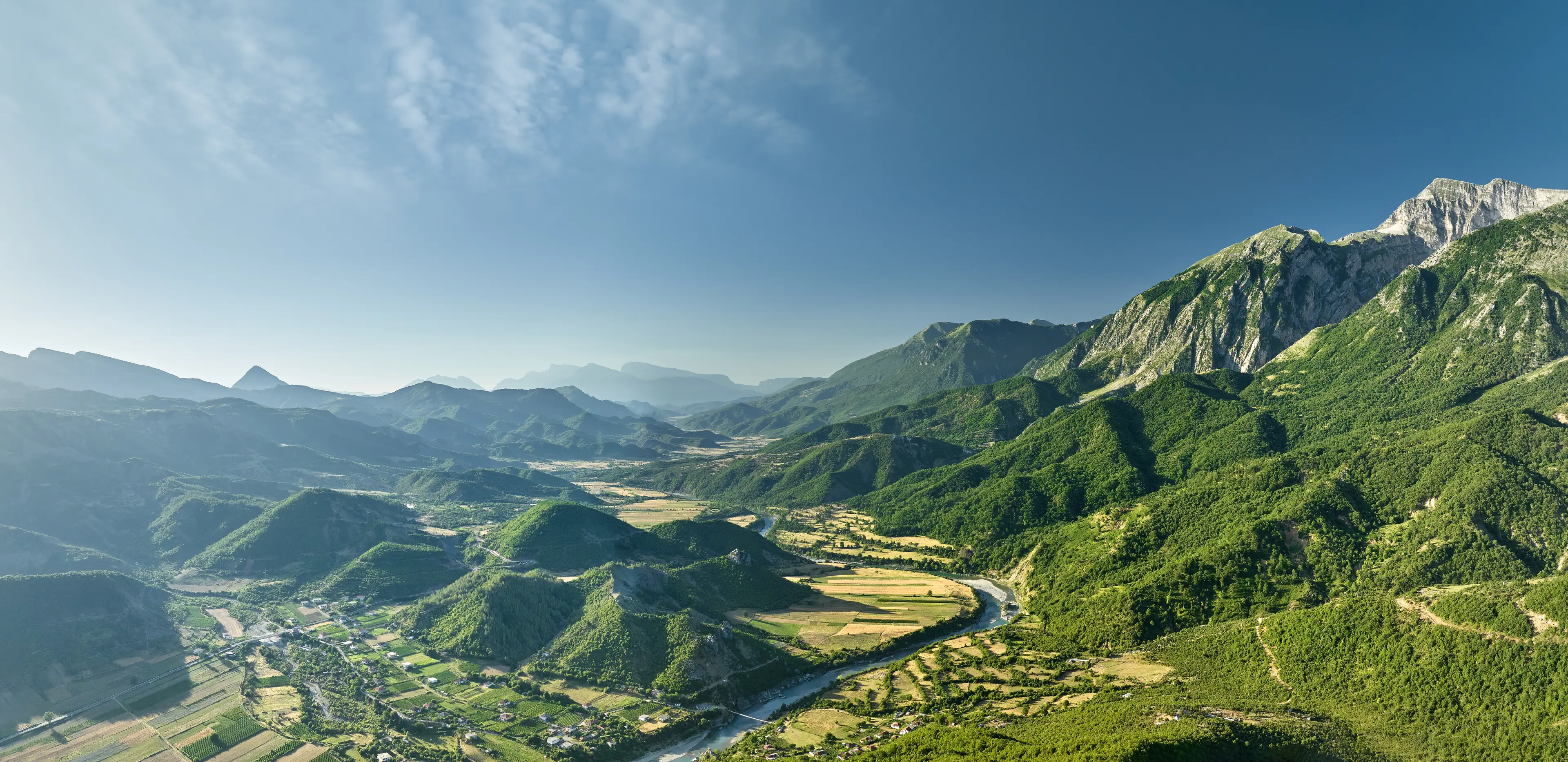 The crystal clear, turquoise river winds its way through fields against a backdrop of majestic mountains.