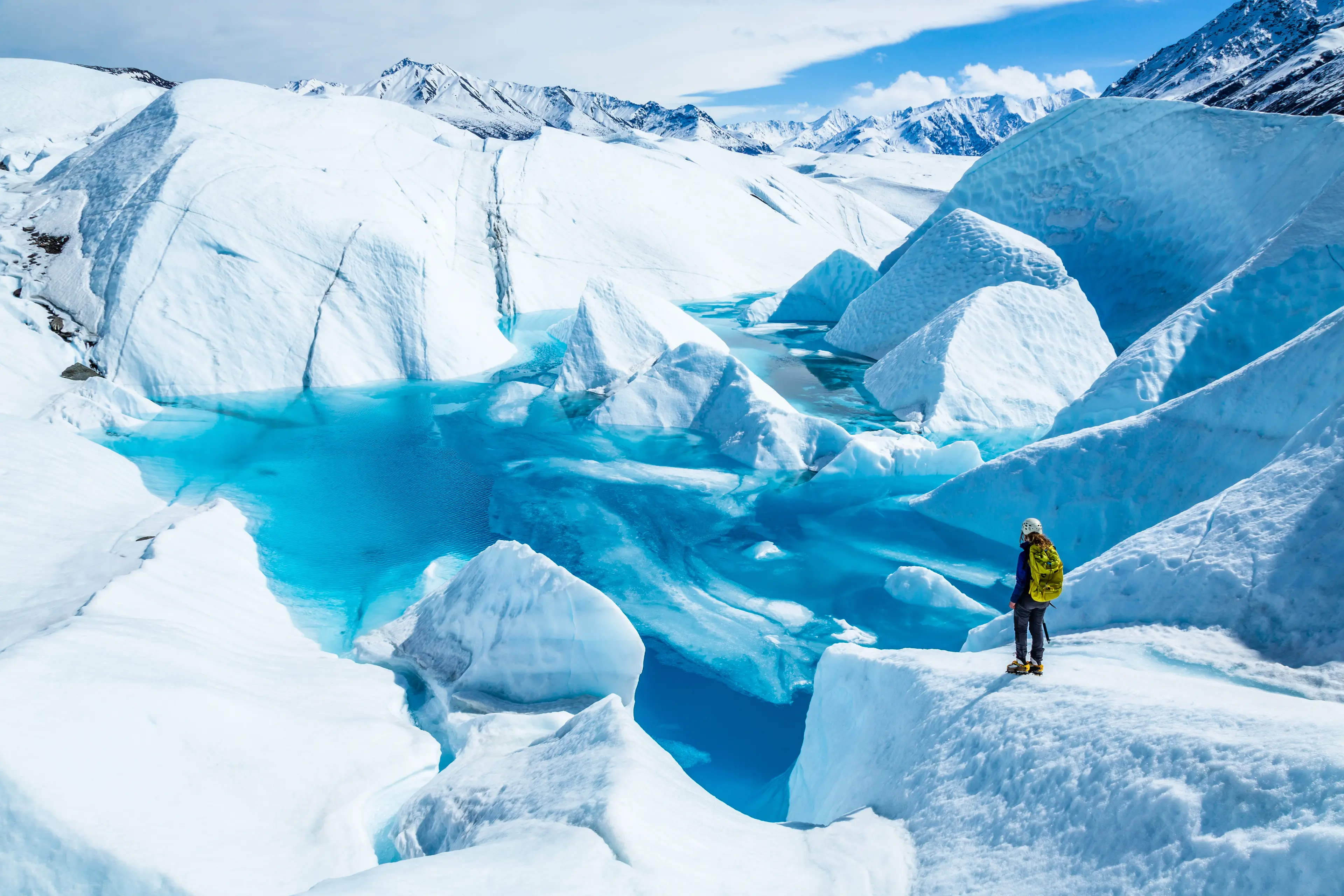 Explorer standing near a clear blue lake on the Matanuska Glacier